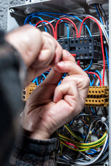 Electrician with screwdriver fixes the cable in a residential electrical distribution panel....
