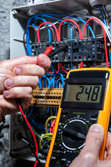 Electrician with multimeter tester measures the voltage in a residential distribution electrical panel. Construction industry, electrical system.