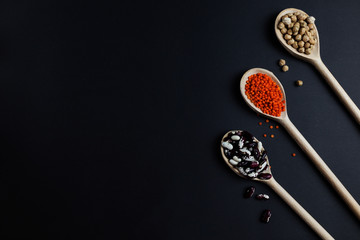Lentils chickpeas and beans on a dark background in wooden spoons