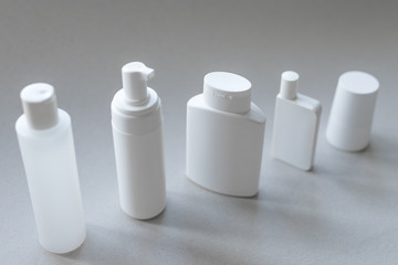 Diagonally placed white plastic cosmetic containers for body care on a gray background