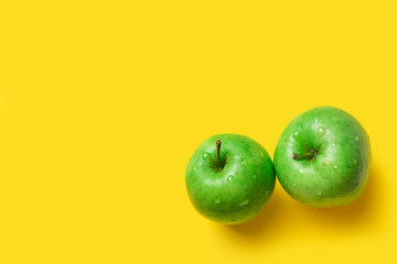 two natural juicy green apples on a yellow background