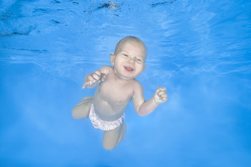 Little baby girl learns to swims underwater. Girl swimming underwater in the pool on a blue water background. Healthy family lifestyle and children water sports activity.