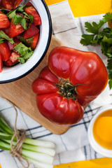 Giant fleshy ripe red tomato on a wooden Board, tomato and green salad in a plate. Vegetable menu, vegetarian menu.