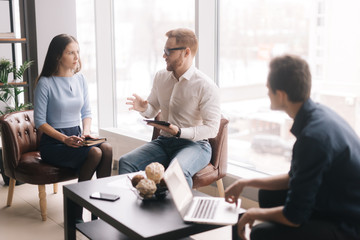Three friendly business man and woman colleagues in formalwear working using laptop and talking in office room. Three colleagues men and woman are cooperating in boardroom.Concept of office life.