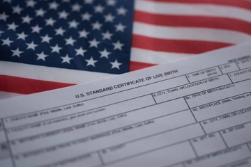 U.S. standard certificate of live birth application form next to flag of USA. Birthright citizenship concept.