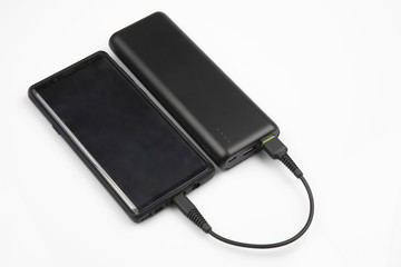 powerbank charges a smartphone battery on a white background. digital technologies and devices