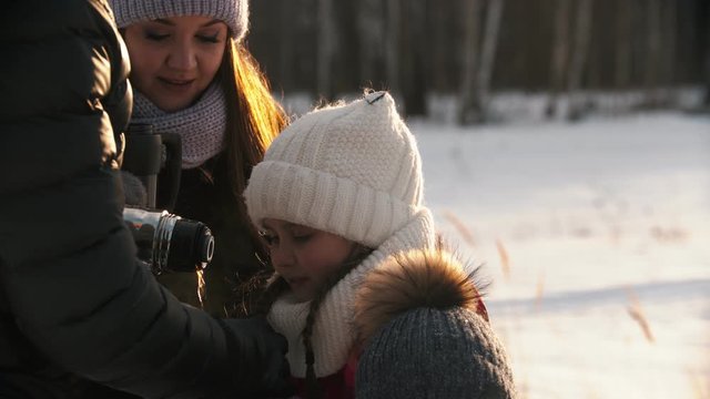 Family drinking hot drinks from the termos in winter time - sunset