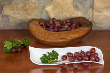 Raw gooseberries (lat. Ribes uva-crispa) in wooden bowl photographed on dark wood with natural light