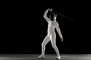 Invincible. Teen girl in fencing costume with sword in hand isolated on black background. Young...