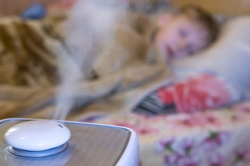 steam flow from a humidifier and an air ionizer in a blurred room with a sleep small child. Climatic device used to increase indoor humidity. respiratory disease prevention