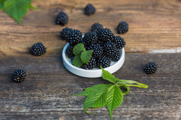 Ripe blackberries with leaves in a bowl on a woodenk background