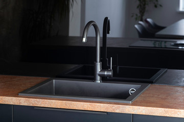Black kitchen sink with black mixer in a kitchen with black fronts, black handles and black glossy backsplash with copper look countertop. 