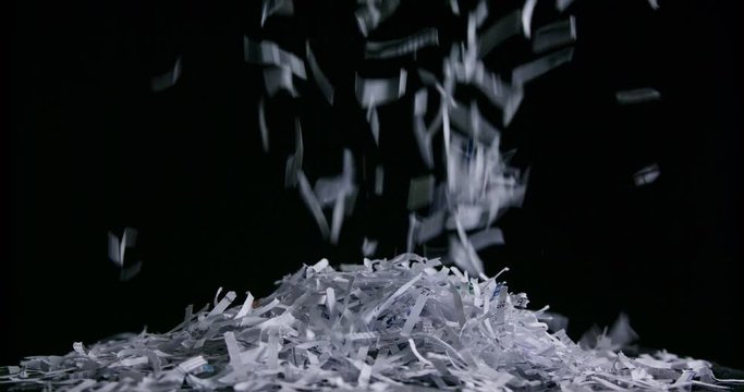 Shredded paper pieces falling against black background forming a mound of waste
