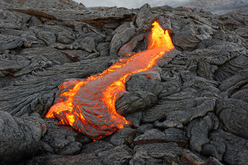 Hot magma of an active lava flow emerges from a rock fissure, the glowing lava makes the air...
