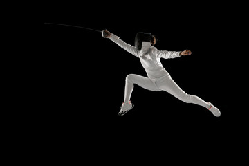 Fototapeta na wymiar Invincible. Teen girl in fencing costume with sword in hand isolated on black background. Young female model practicing and training in motion, action. Copyspace. Sport, youth, healthy lifestyle.