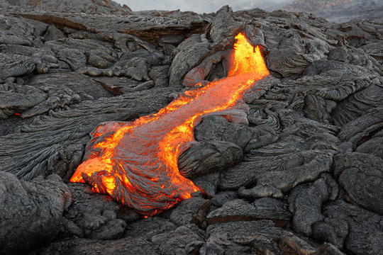 Hot magma of an active lava flow emerges from a rock fissure, the glowing lava makes the air flicker with heat, the lava cools down slowly and solidifies in bizarre patterns - Hawaii, Kilauea