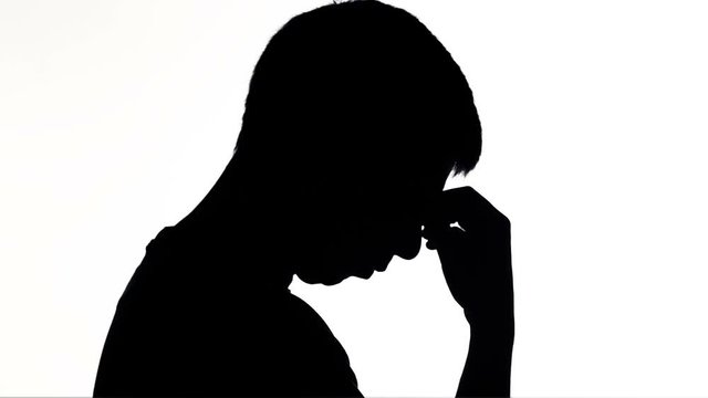 silhouette of a young sad man holding forehead on hand, boy thinking solving a problem, concept of emotion and life