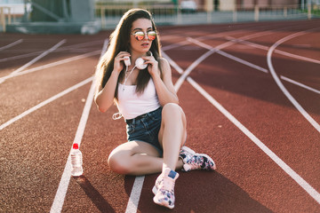 Stylish woman posing for the camera sitting on running track.