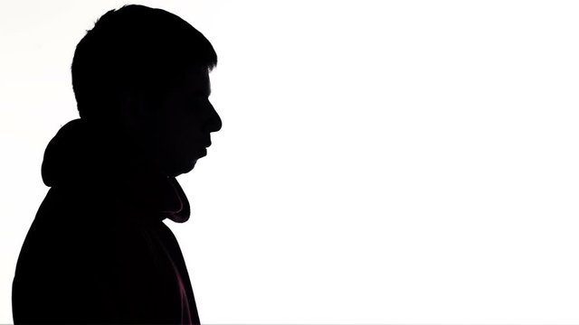 silhouette of a young man puts on a hood of a sweatshirt and goes on white isolated background, unknown person, guy hides face, concept fashion