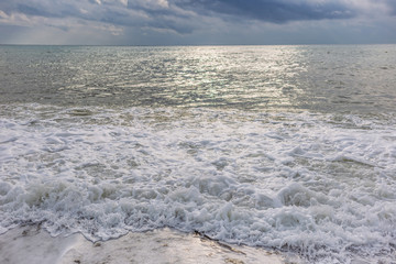 Beautiful sunny surface of sea water splashing at beach and dramatic cloudy grey rainy sky. Turkish seascape.