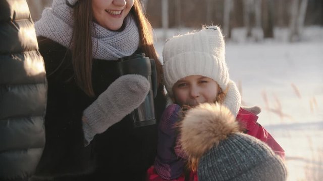 Family of four people drinking hot drinks from the termos in winter time - a little girl laughing