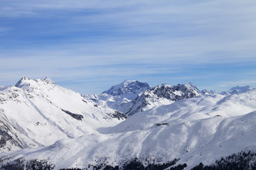 Snowy slope in high winter mountains and blue sunlit cloudy sky