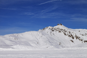 Fototapeta na wymiar Snowy ski slope at high winter mountains and sunlit blue sky