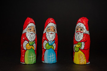 3 Weihnachtsmänner vor schwarzem Hintergrund, linklsseitig, aus Schokolade, gleich aussehend, weißer Bart