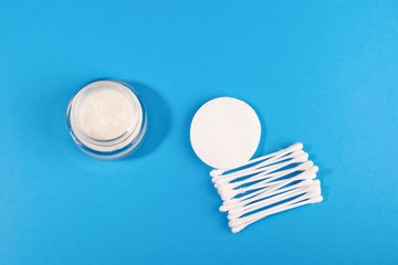 white cosmetic cream in a jar, cotton swabs and a disk on a blue background
