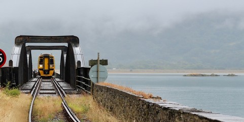 Train crossing the Mawddach estuary on Barmouth railway bridge on a grey cloudy day wide crop