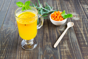Fragrant tea with sea buckthorn and mint leaves on a dark wooden table. Healthy drink