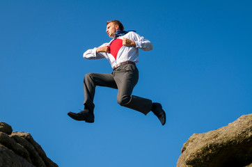 Obraz premium Superhero businessman jumping outdoors in sunny blue sky between two rocks