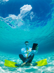Snorkelling businessman in shirt and tie and matching fins using a tablet computer sitting...