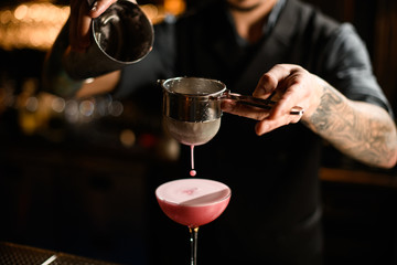 Close-up of bartender pouring cocktail with shaker and sieve