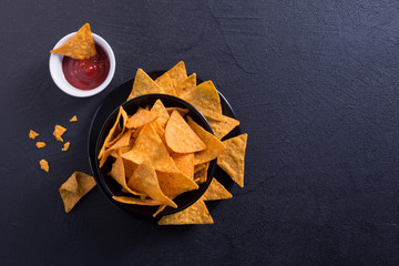 Traditional mexican appetizer nachos in a black plate with chili sauce on a black background.