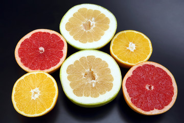 Fototapeta na wymiar cut pieces of different citrus fruits on dark background