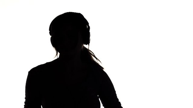 silhouette of a young happy woman listening to music in big headphones and holding a smartphone, girl dancing on white isolated background, concept lifestyle