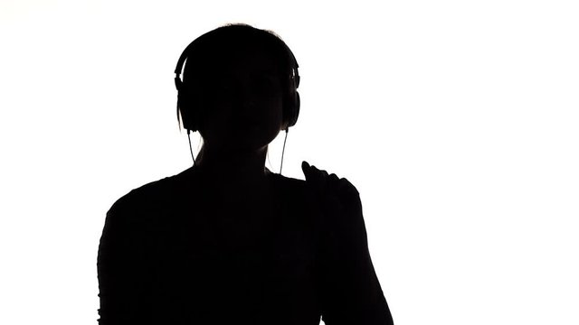 silhouette of a young happy woman listening to music in big headphones and holding a smartphone, girl dancing on white isolated background, concept lifestyle