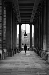 A person walking along a corridor surrounded by architectural columns of a historic building having as a background a set of modern buildings