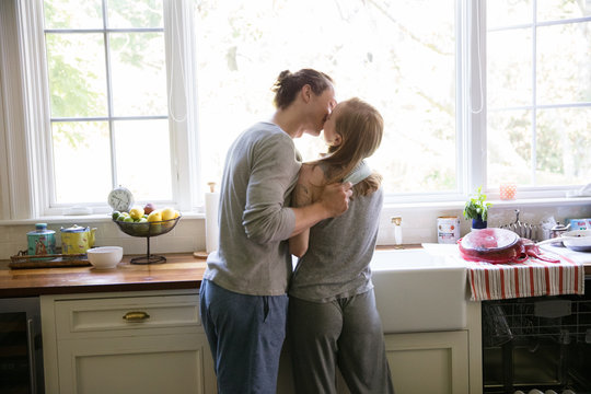 straight caucasian millennials couple in the kitchen kissing and washing dishes in the morning making breakfast
