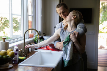 straight caucasian millennials couple in the kitchen kissing and washing dishes in the morning making breakfast