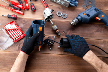 the master repairs a broken electrical device: drill, cutter on a wooden table. Electric Tool...