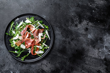 Salad with Serrano jamon, ham, rucola and Parmesan cheese. Black background, top view, space for text