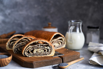 Rosy roll with poppy seeds and milk on a concrete background.