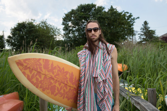 long haired millennial guy with surfboard on dock