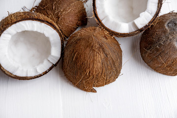 Fototapeta na wymiar Close-up of a broken coconut fruit on a white wooden background with a place for inscription. Banner for spa center, healthy diet, coconut oil for food and body.