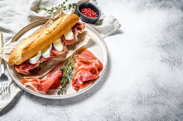 Baguette sandwich with prosciutto ham, Camembert cheese on a plate. Gray background, top view,...