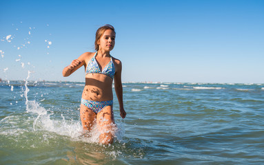 Portrait of a joyful little positive girl swimming in the sea on a sunny warm summer day. The concept of happy children having a rest at the sea. Advertising space