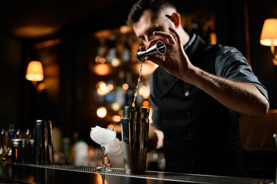 Male bartender flows alcohol from small jigger to shaker