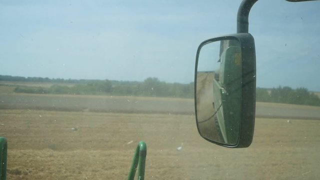 Combine working at wheat field, rearview mirror